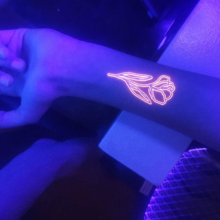 Tatouage temporaire hyperréaliste Glow in the Dark Peace & Flowers - Pack de ArtWear Tattoo Fluorescents & Phosphorescents sur le bras d'un homme et jambe d'une femme