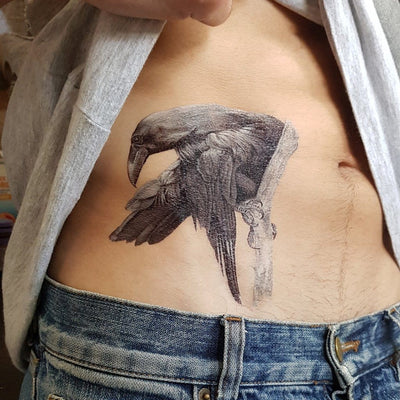 Tatouage temporaire hyperréaliste Black Raven - White Touch de ArtWear Tattoo Animaux sur le bras d'un homme et jambe d'une femme