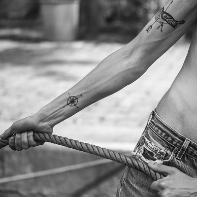 Tatouage temporaire hyperréaliste Small Compass de ArtWear Tattoo Minimalistes sur le bras d'un homme et jambe d'une femme