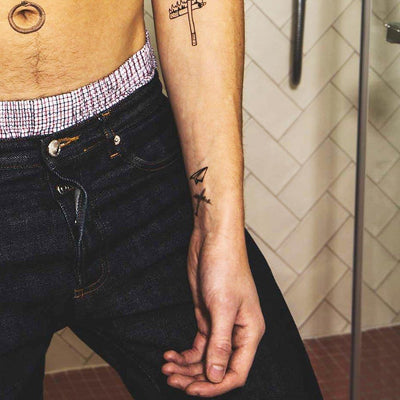 Tatouage temporaire hyperréaliste Wanderlust de ArtWear Tattoo Minimalistes sur le bras d'un homme et jambe d'une femme