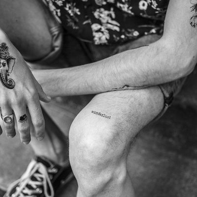Tatouage temporaire hyperréaliste Wanderlust de ArtWear Tattoo Minimalistes sur le bras d'un homme et jambe d'une femme